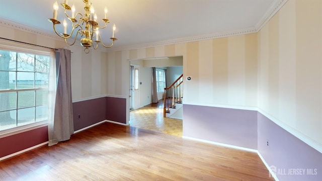 empty room featuring hardwood / wood-style flooring, a notable chandelier, ornamental molding, and a wealth of natural light