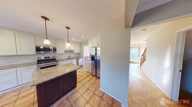 kitchen with appliances with stainless steel finishes, light stone counters, white cabinets, decorative light fixtures, and tasteful backsplash