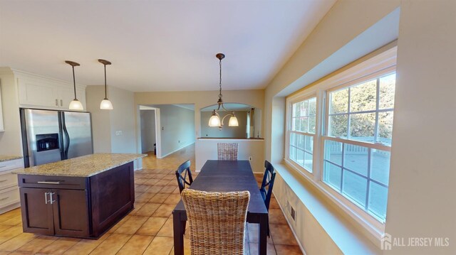 kitchen featuring light stone countertops, light tile patterned floors, stainless steel fridge, white cabinets, and decorative light fixtures