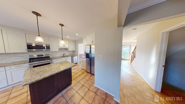 kitchen featuring appliances with stainless steel finishes, pendant lighting, white cabinetry, and light stone countertops