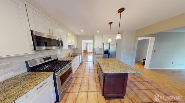 kitchen featuring stainless steel appliances, white cabinetry, backsplash, hanging light fixtures, and light stone countertops