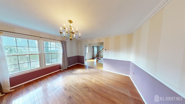 empty room featuring hardwood / wood-style floors, ornamental molding, and a notable chandelier