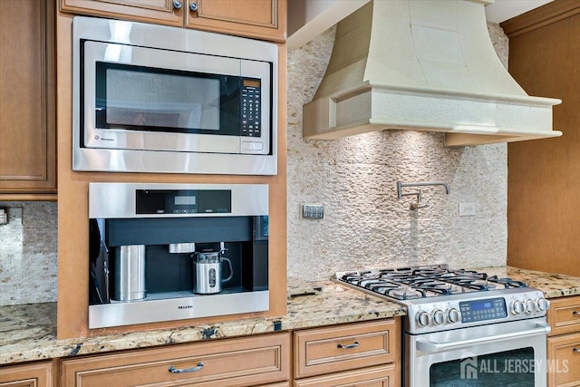 kitchen with light stone counters, tasteful backsplash, premium range hood, and appliances with stainless steel finishes