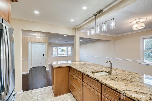 kitchen with a healthy amount of sunlight, light stone countertops, brown cabinetry, freestanding refrigerator, and a sink