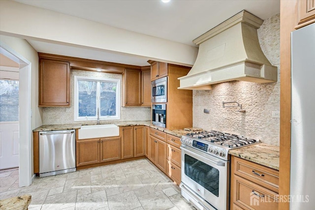 kitchen with light stone counters, appliances with stainless steel finishes, custom exhaust hood, stone finish floor, and a sink