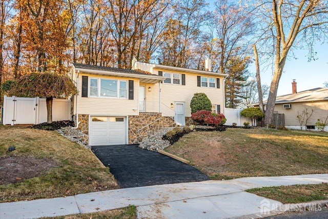 split level home with a front yard, fence, an attached garage, stone siding, and aphalt driveway