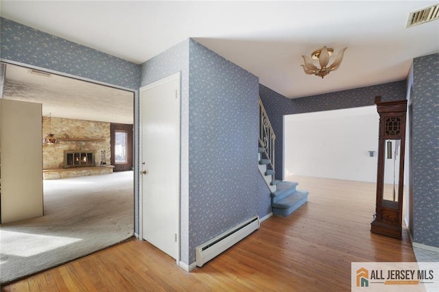 hall with wallpapered walls, stairs, visible vents, and a baseboard heating unit