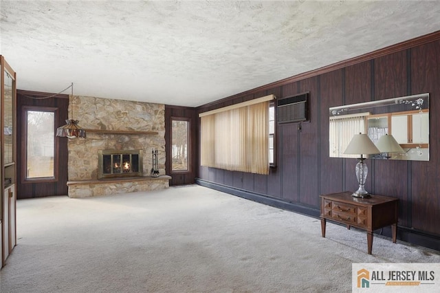 unfurnished living room with carpet floors, a textured ceiling, a stone fireplace, and wooden walls