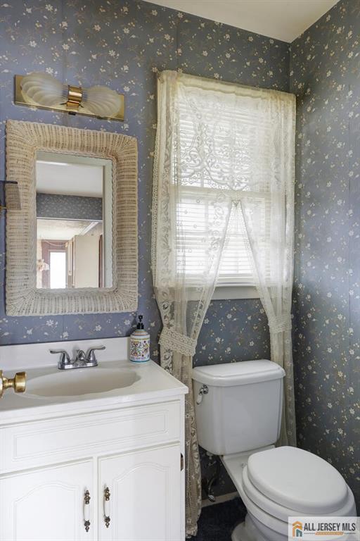 bathroom featuring toilet, vanity, and wallpapered walls