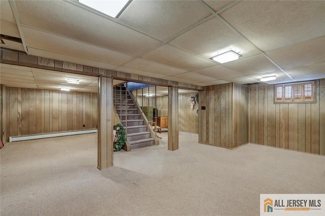 below grade area featuring stairway, a drop ceiling, wooden walls, and a baseboard radiator