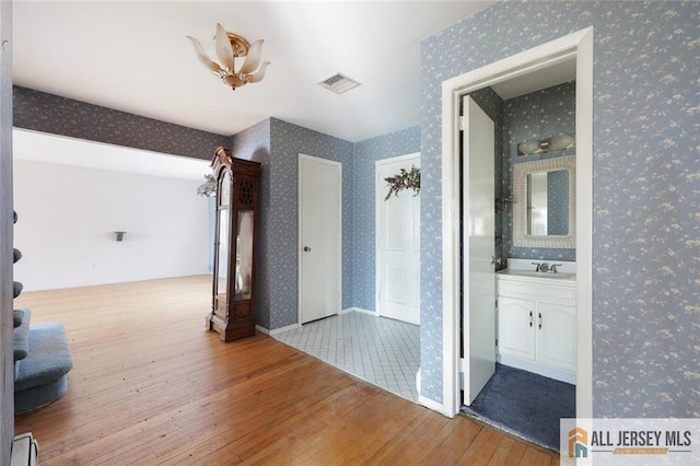 hallway with visible vents, hardwood / wood-style flooring, a sink, wallpapered walls, and baseboard heating