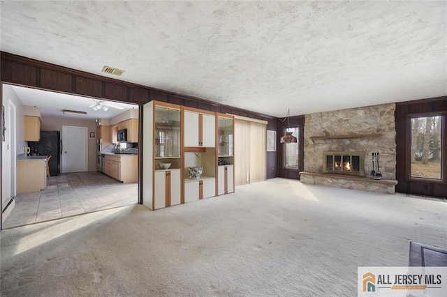 unfurnished living room featuring a stone fireplace, light colored carpet, visible vents, and a textured ceiling