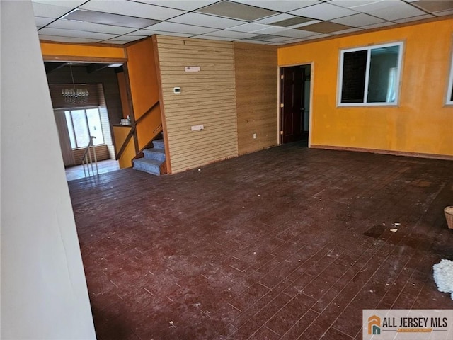 empty room featuring a notable chandelier, wood walls, and a drop ceiling