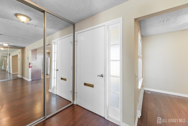 hall with visible vents, a textured ceiling, baseboards, and wood finished floors