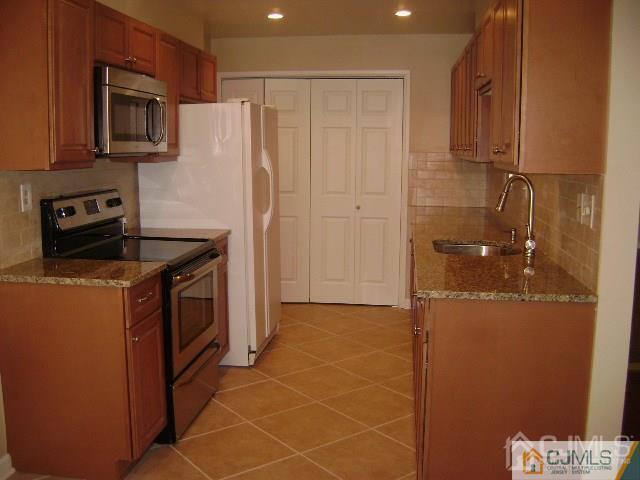 kitchen with sink, light tile patterned floors, stainless steel appliances, light stone countertops, and backsplash