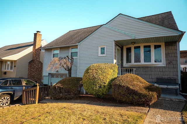 view of front of house with an attached garage, roof with shingles, and a front yard