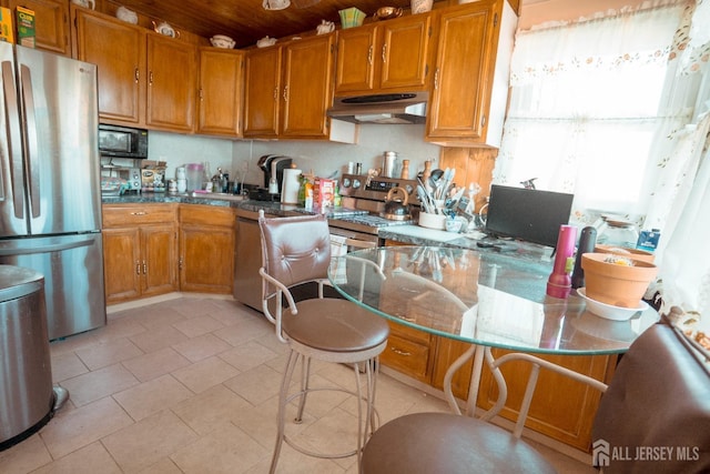 kitchen featuring light tile patterned floors, appliances with stainless steel finishes, brown cabinetry, and under cabinet range hood