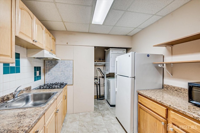 kitchen with open shelves, a sink, freestanding refrigerator, stacked washer / dryer, and gas stovetop