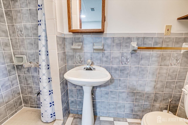 bathroom featuring visible vents, toilet, tiled shower, and tile walls