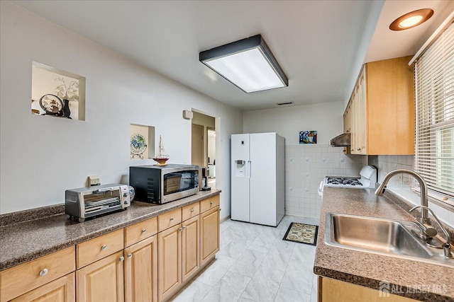 kitchen featuring exhaust hood, light brown cabinetry, white refrigerator with ice dispenser, a sink, and stainless steel microwave