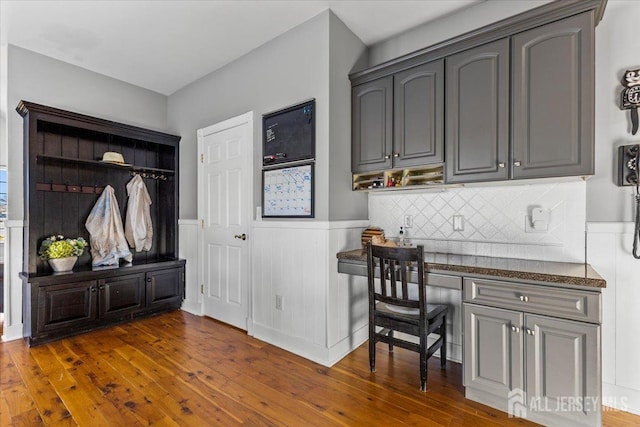 mudroom featuring built in study area, wainscoting, and dark wood-type flooring