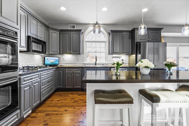 kitchen featuring a breakfast bar area, a sink, appliances with stainless steel finishes, gray cabinets, and dark countertops