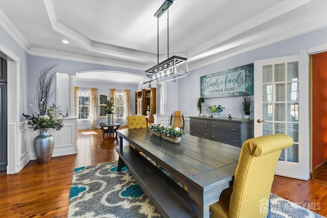 dining area featuring arched walkways, hardwood / wood-style flooring, a wainscoted wall, ornamental molding, and ornate columns