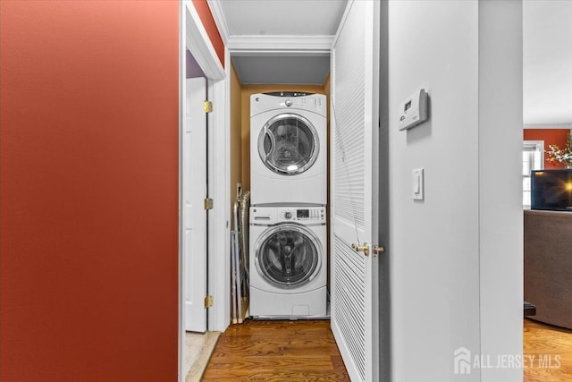 clothes washing area with laundry area, crown molding, stacked washer / drying machine, and wood finished floors