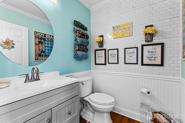 half bath featuring toilet, vanity, ornamental molding, and wainscoting