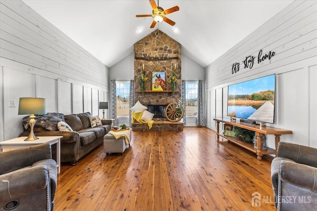 living room featuring ceiling fan, high vaulted ceiling, a stone fireplace, and hardwood / wood-style flooring