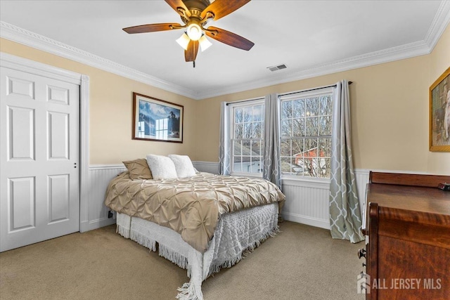 carpeted bedroom featuring ceiling fan, visible vents, wainscoting, and ornamental molding