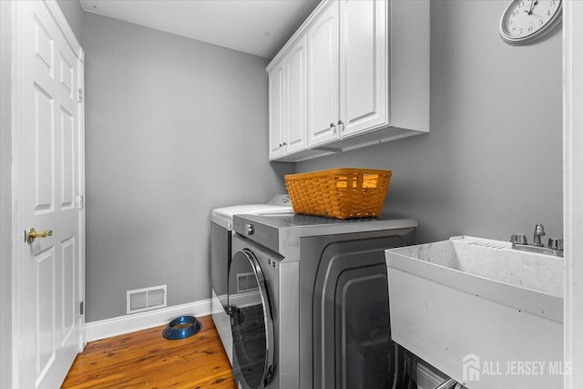 clothes washing area with cabinet space, a sink, wood finished floors, visible vents, and washing machine and dryer