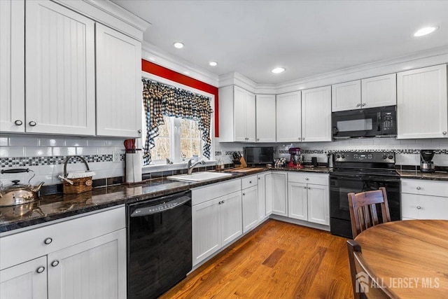 kitchen with a sink, backsplash, black appliances, and white cabinetry