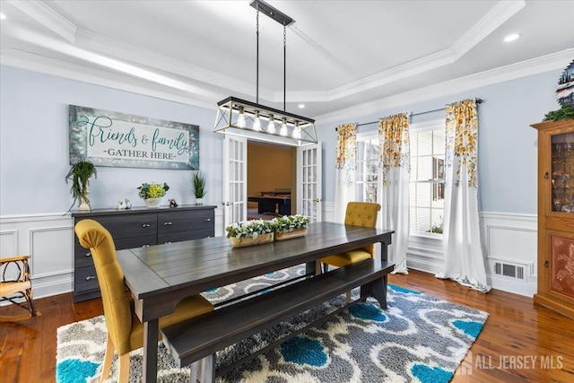 dining room with visible vents, wood finished floors, a wainscoted wall, ornamental molding, and a tray ceiling