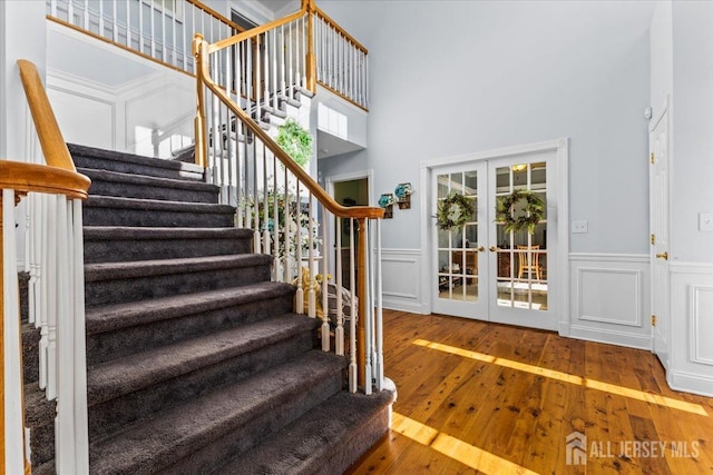 stairway with a wainscoted wall, french doors, hardwood / wood-style flooring, and a decorative wall