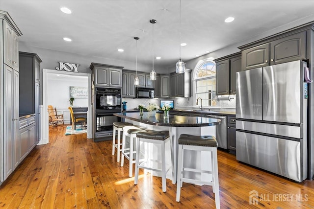 kitchen featuring a kitchen island, a breakfast bar, dark wood-style floors, black appliances, and gray cabinetry