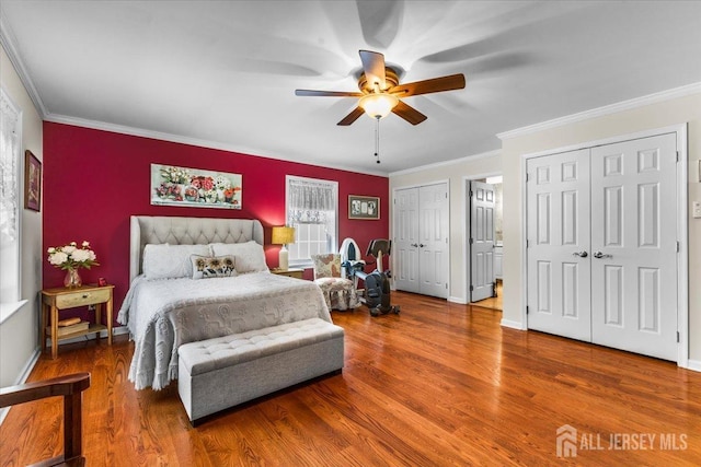 bedroom with two closets, ceiling fan, ornamental molding, and wood finished floors