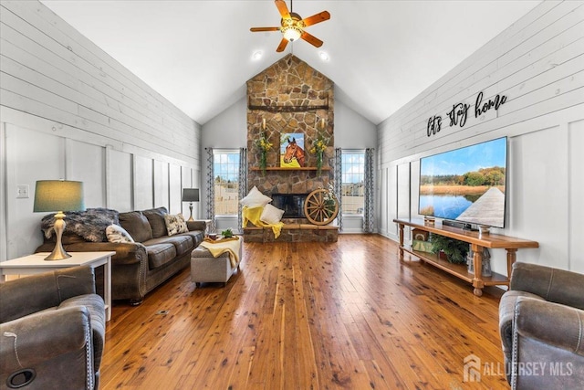 living room with high vaulted ceiling, wood walls, a ceiling fan, and hardwood / wood-style flooring