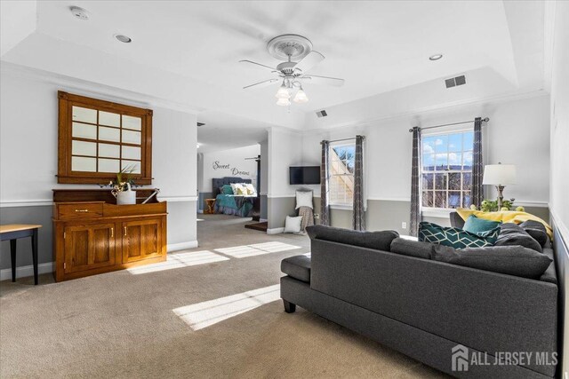 living area with carpet floors, visible vents, a raised ceiling, and a ceiling fan