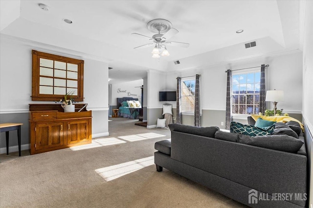 carpeted living area featuring a ceiling fan, a tray ceiling, visible vents, and baseboards