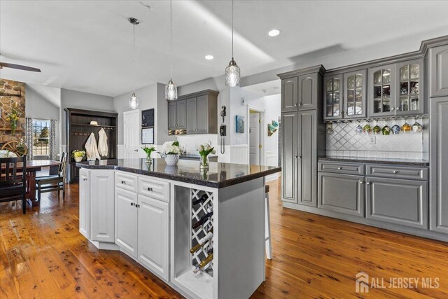 kitchen with decorative backsplash, glass insert cabinets, dark wood-style flooring, a center island, and gray cabinetry