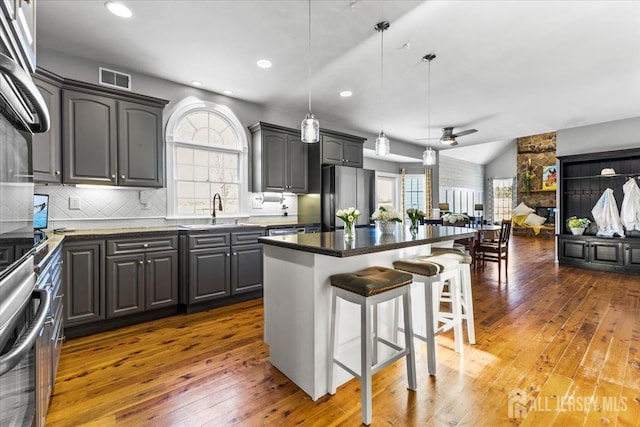 kitchen with freestanding refrigerator, hardwood / wood-style floors, a kitchen bar, a sink, and vaulted ceiling