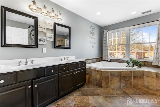 bathroom featuring visible vents, a garden tub, double vanity, recessed lighting, and a sink