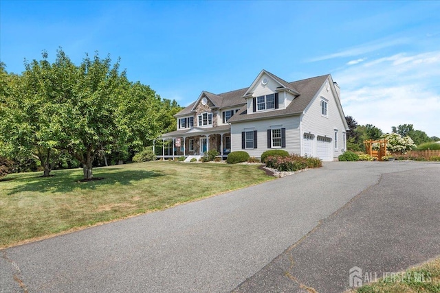 view of front of property with an attached garage, aphalt driveway, covered porch, and a front yard