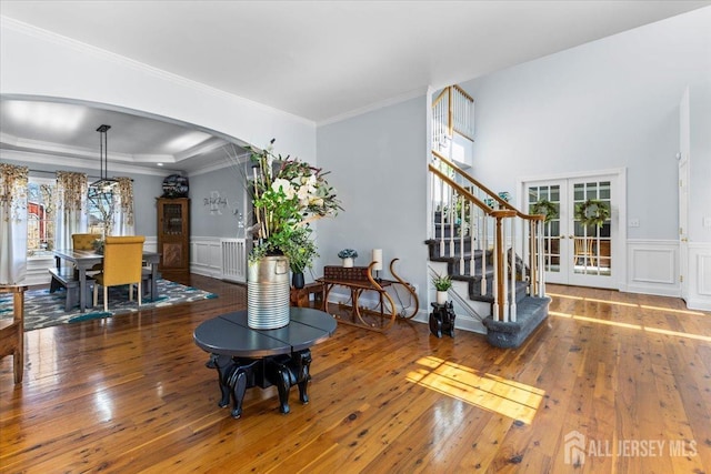 living room featuring wood-type flooring, ornamental molding, stairs, a wainscoted wall, and arched walkways