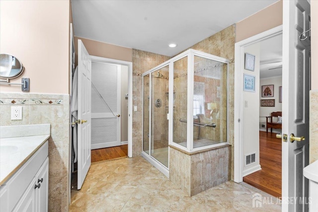 full bath featuring vanity, a shower stall, visible vents, and tile walls