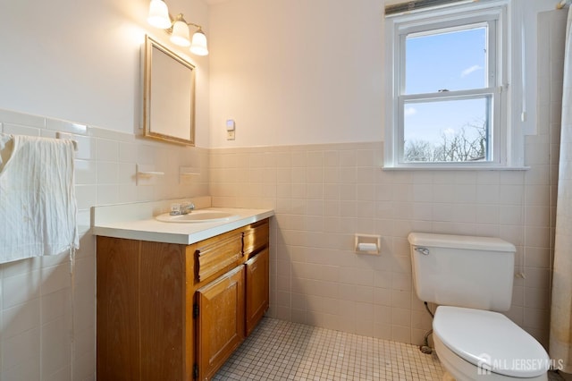 bathroom with toilet, tile walls, vanity, wainscoting, and tile patterned floors