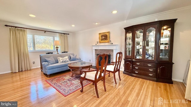 sitting room featuring light wood-type flooring, a fireplace, baseboards, and crown molding