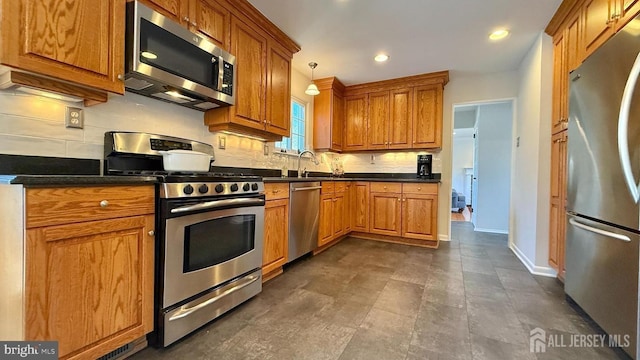 kitchen with appliances with stainless steel finishes, dark countertops, brown cabinetry, and decorative light fixtures