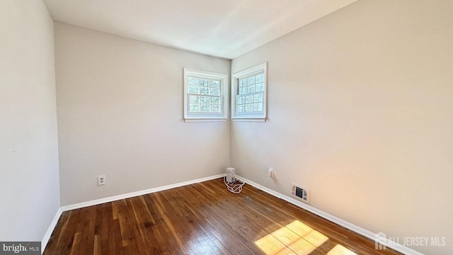 empty room with wood-type flooring, visible vents, and baseboards